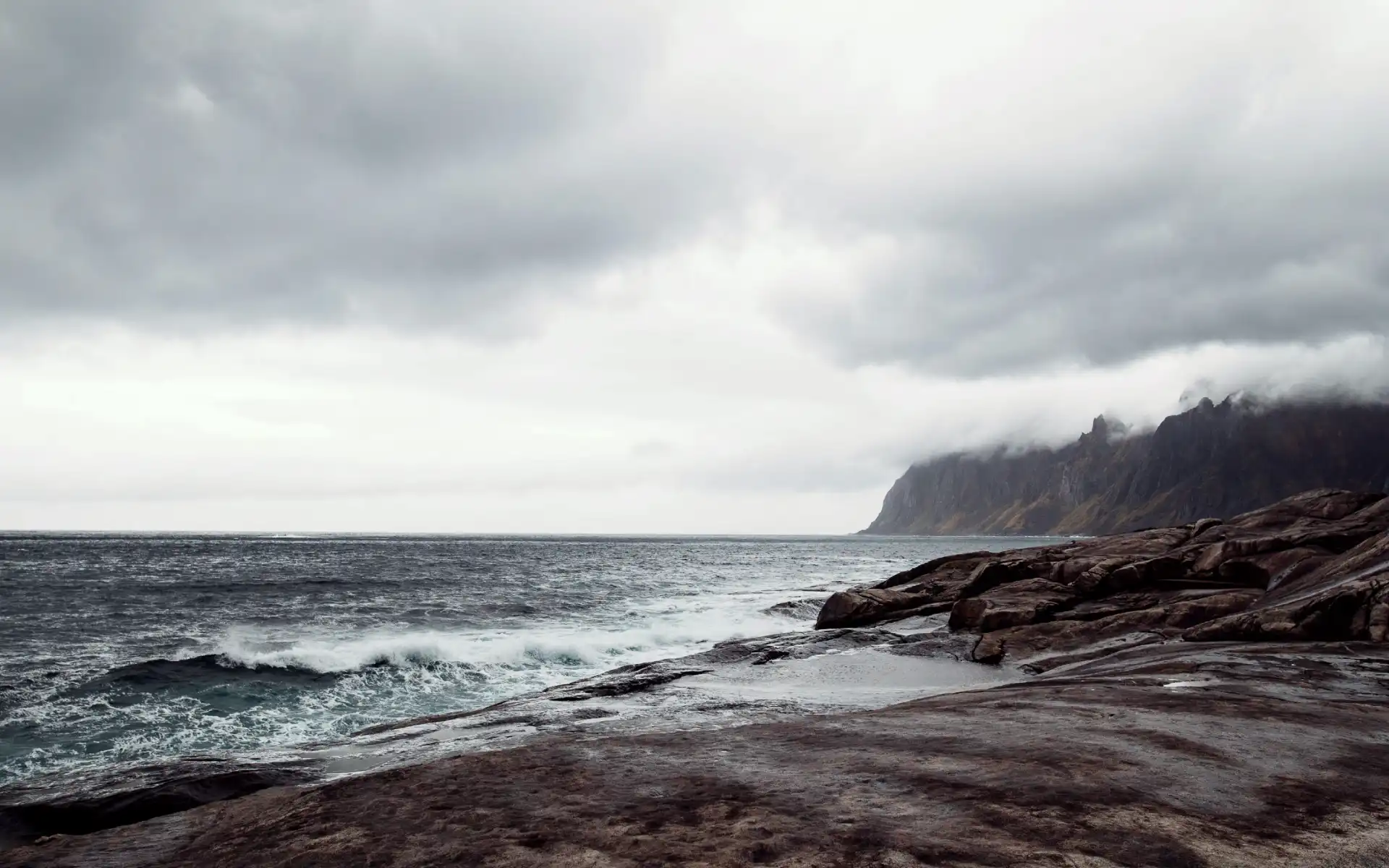 Rugged coastline with crashing waves and mist-covered mountains in the background, capturing the raw power of nature and potential for renewable energy.