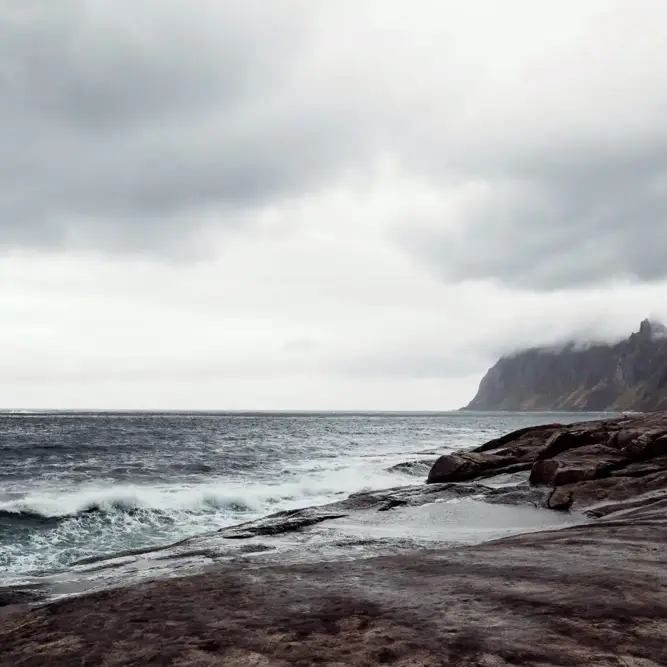 Rugged coastline with crashing waves and mist-covered mountains in the background, capturing the raw power of nature and potential for renewable energy.