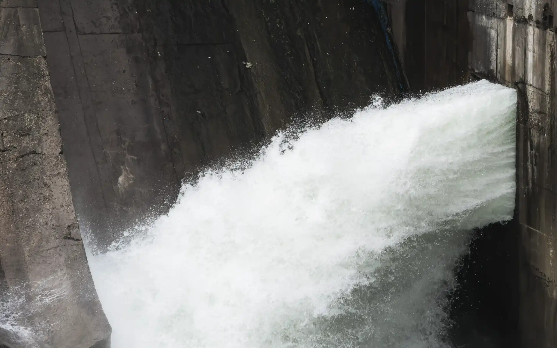 Close-up of water gushing through a concrete sluice gate in a hydroelectric power station.