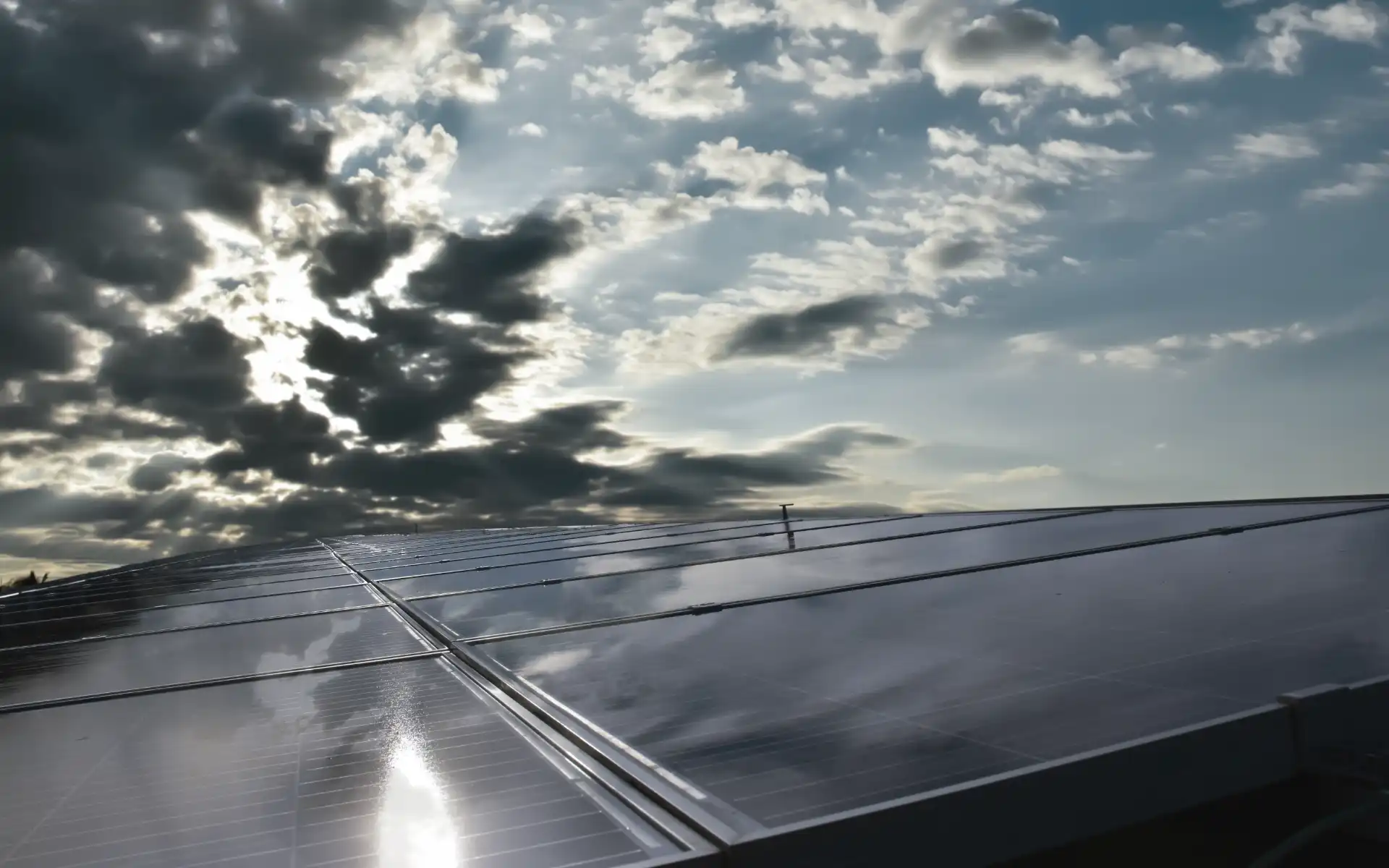 Close-up of reflective solar panels on a rooftop with sunlight breaking through the clouds.