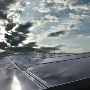 Close-up of reflective solar panels on a rooftop with sunlight breaking through the clouds.