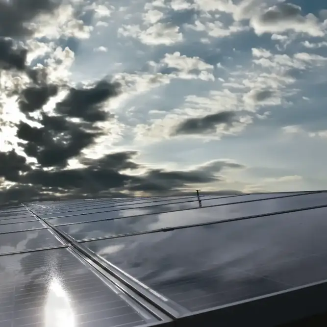 Close-up of reflective solar panels on a rooftop with sunlight breaking through the clouds.