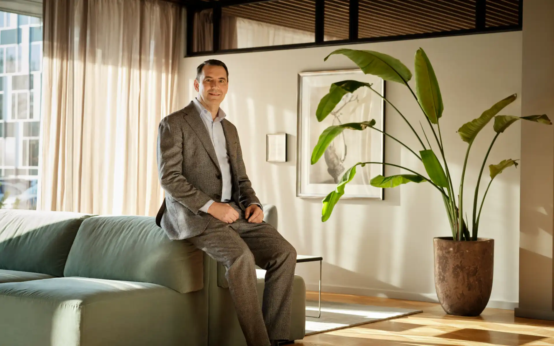 Kenneth Valbøll in a suit sitting on a sofa in a bright, plant-filled energy office lounge