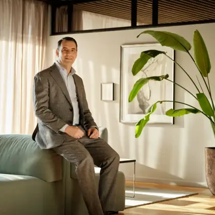 Kenneth Valbøll in a suit sitting on a sofa in a bright, plant-filled energy office lounge