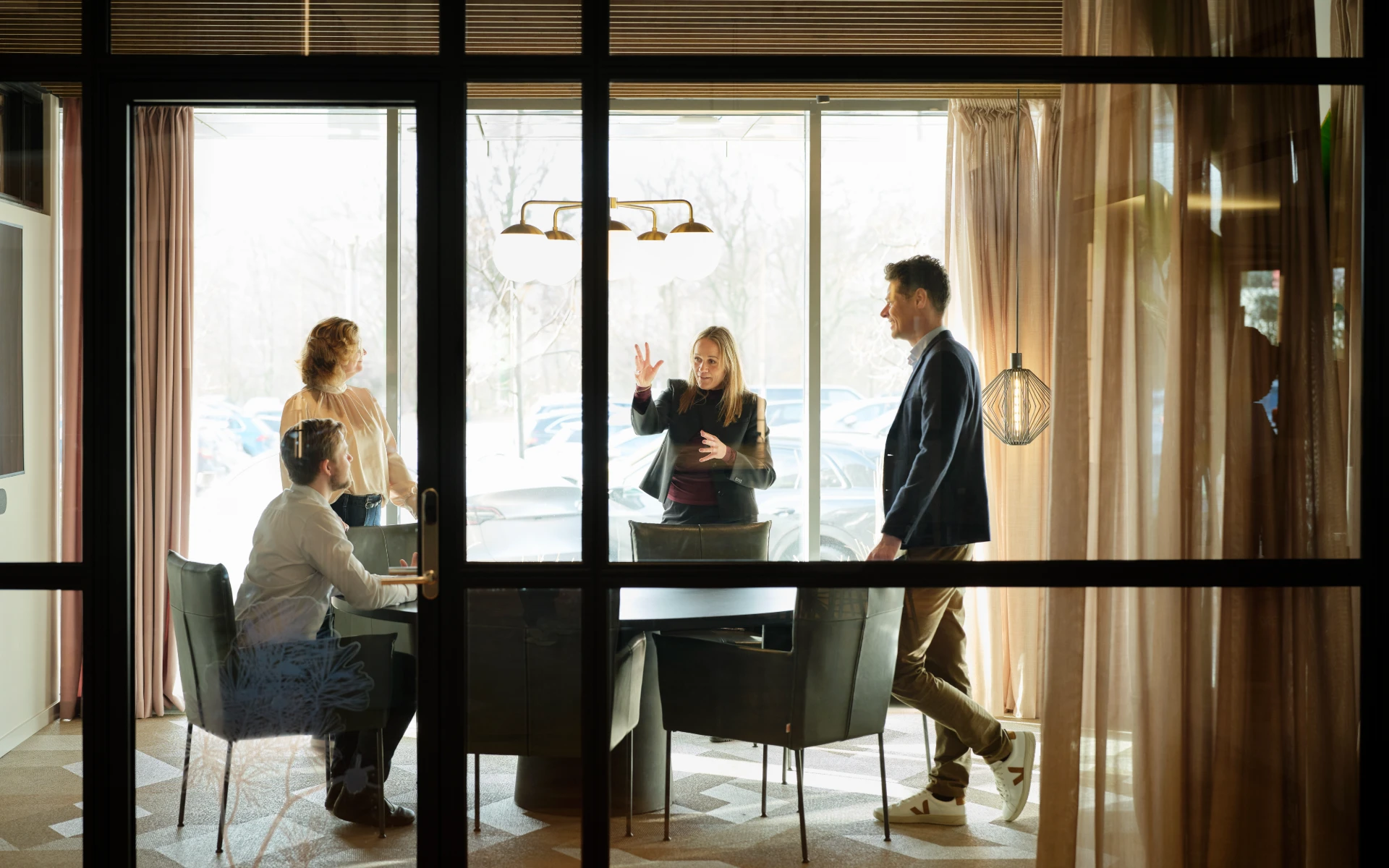 Four team members in discussion around a conference table in a sunlit meeting room.