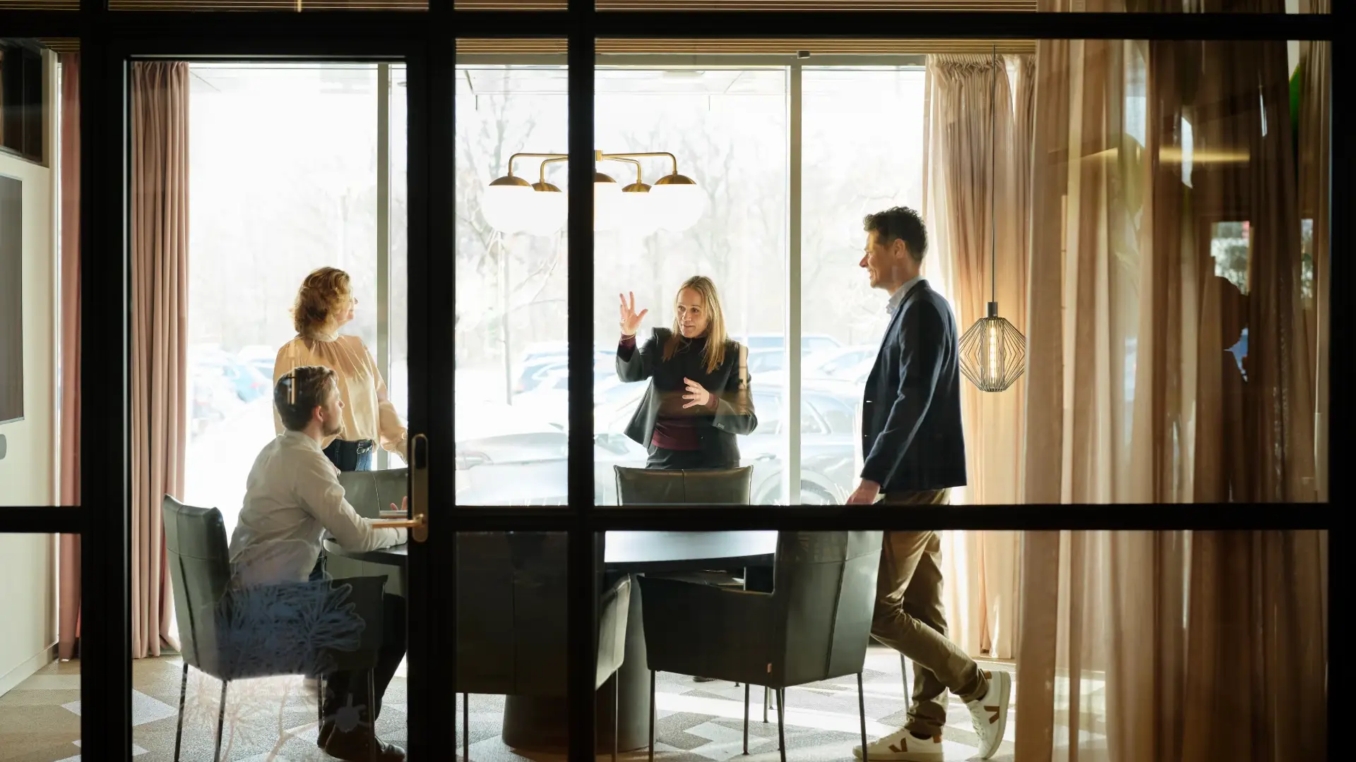 Four team members in discussion around a conference table in a sunlit meeting room.