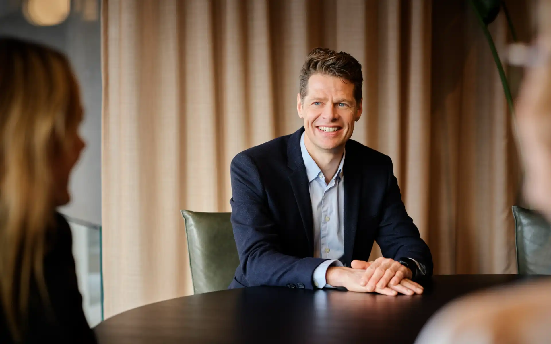 Man in a suit smiling while engaged in a meeting at a round table.