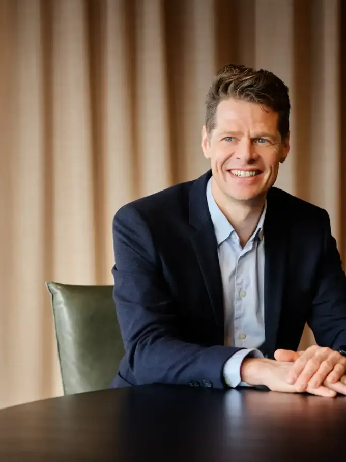 Man in a suit smiling while engaged in a meeting at a round table.