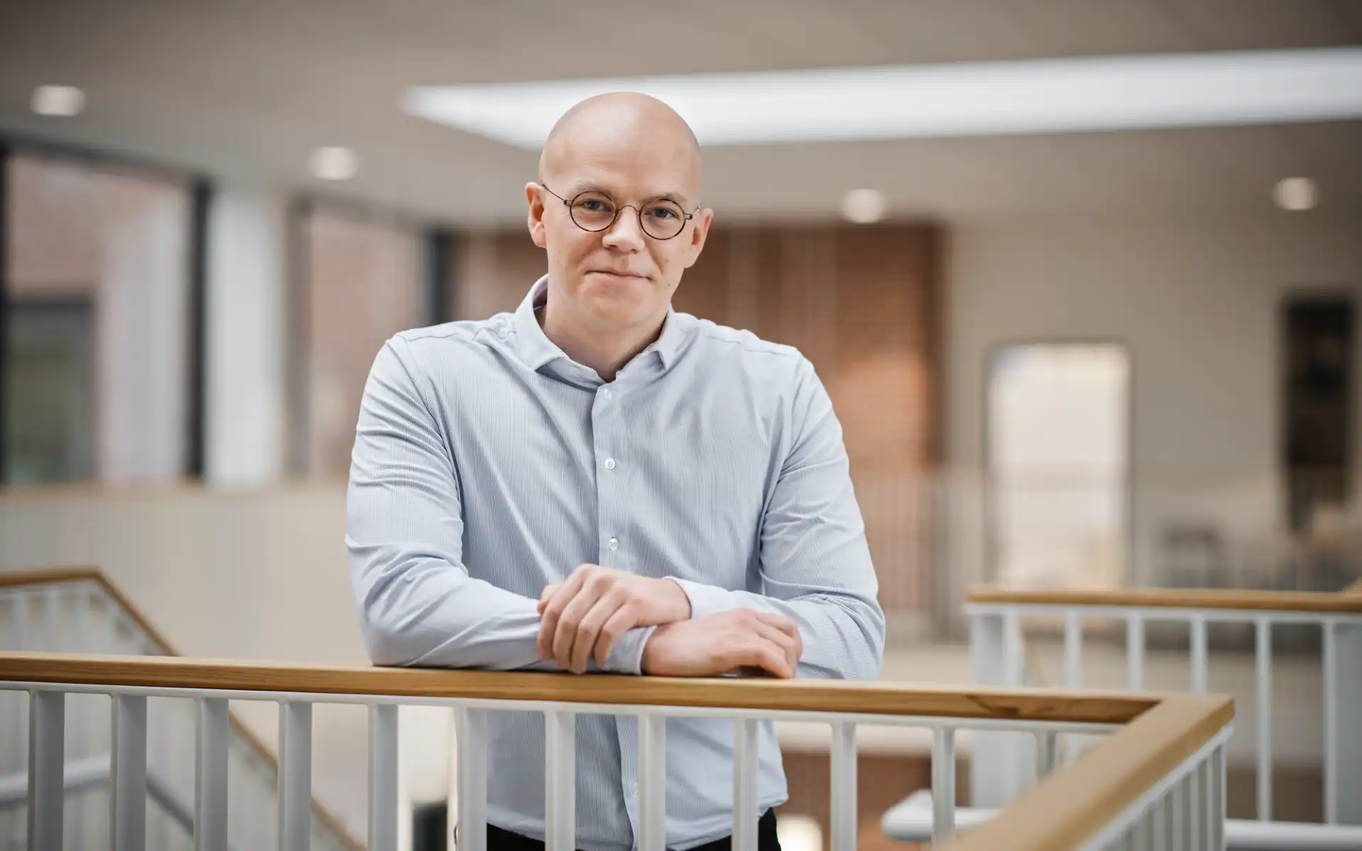 Mads Myrup smiling while leaning on a railing in a bright energy company workspace.