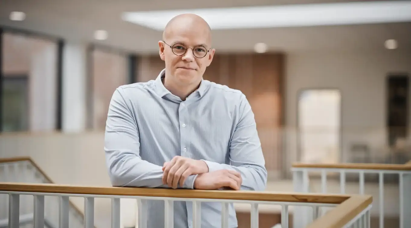 Mads Myrup smiling while leaning on a railing in a bright energy company workspace.