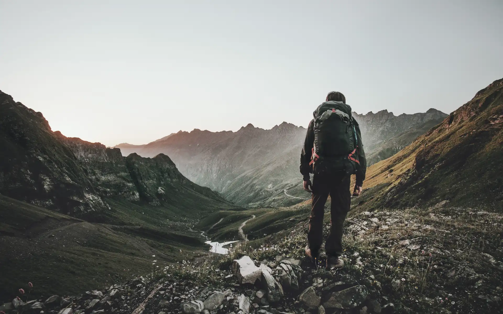 Person with backpack overlooking a vast mountain valley at sunrise, symbolizing sustainable exploration and forward-looking energy solutions.