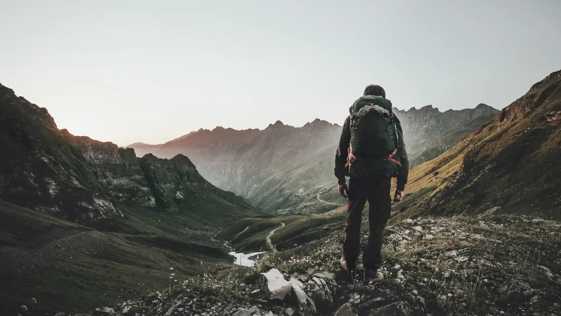 Person with backpack overlooking a vast mountain valley at sunrise, symbolizing sustainable exploration and forward-looking energy solutions.