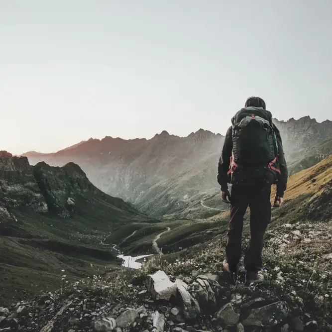 Person with backpack overlooking a vast mountain valley at sunrise, symbolizing sustainable exploration and forward-looking energy solutions.