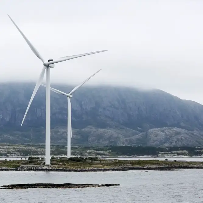 Offshore wind turbines rising above the coastline with misty mountains in the background.