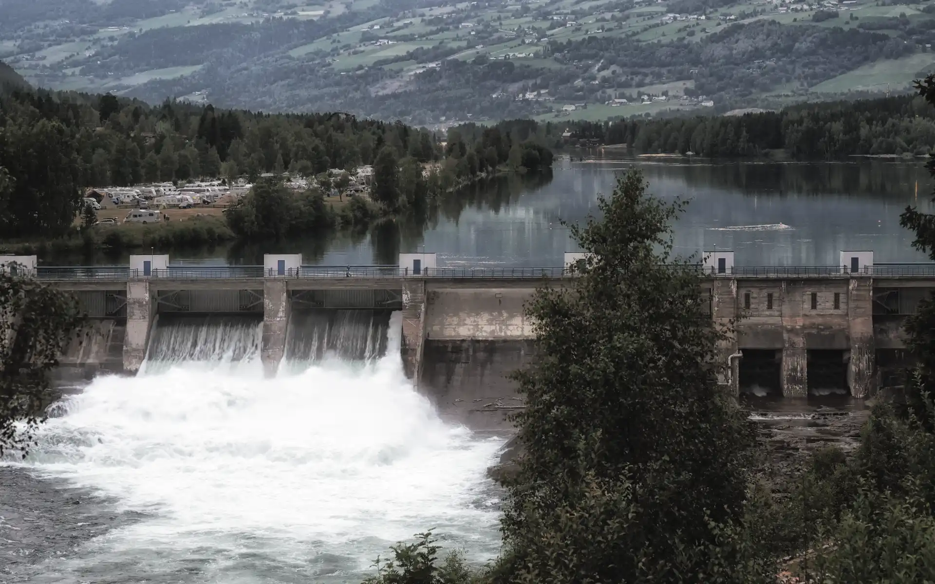 Hydropower dam with rushing water outflow, surrounded by a forested valley 