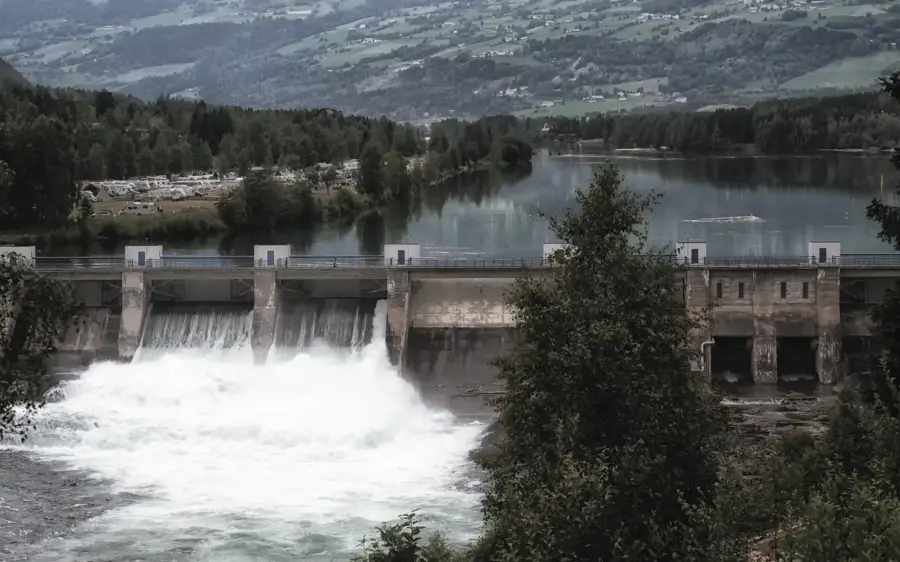 Hydropower dam with rushing water outflow, surrounded by a forested valley 