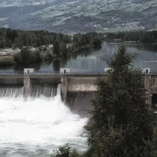 Hydropower dam with rushing water outflow, surrounded by a forested valley