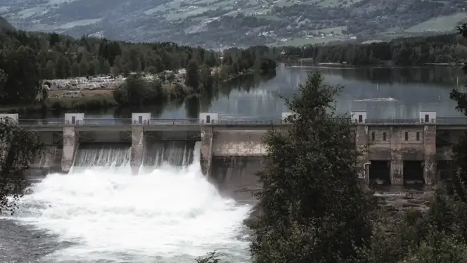 Hydropower dam with rushing water outflow, surrounded by a forested valley