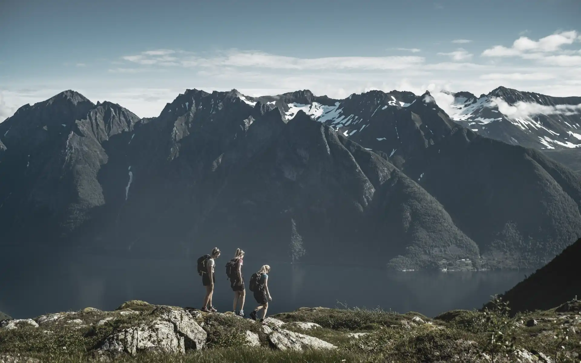 Three hikers walking along a ridge with dramatic mountain peaks and a fjord below, reflecting unity, resilience, and the power of nature in renewable energy.