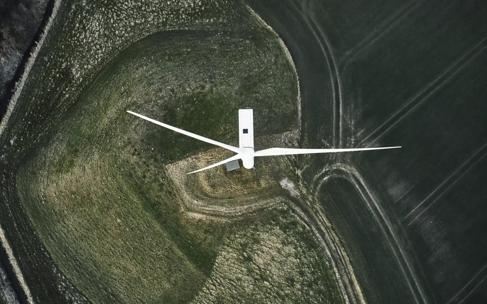 Top-down drone view of a single wind turbine surrounded by agricultural fields.