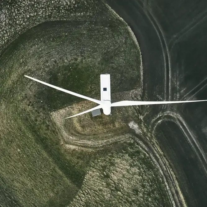 Top-down drone view of a single wind turbine surrounded by agricultural fields.