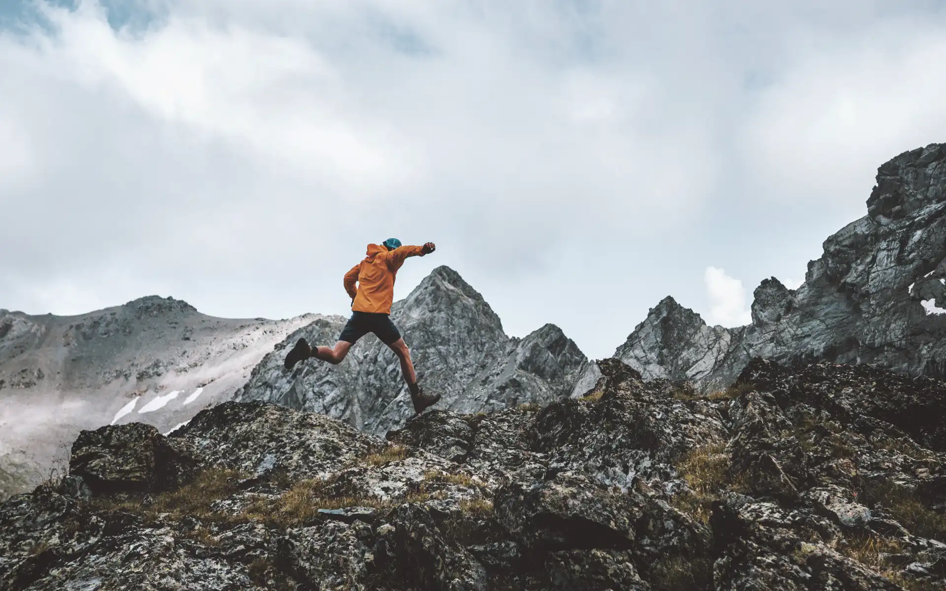 Adventurer jumping between mountain rocks under a cloudy sky, representing bold moves and energy transition in challenging environments