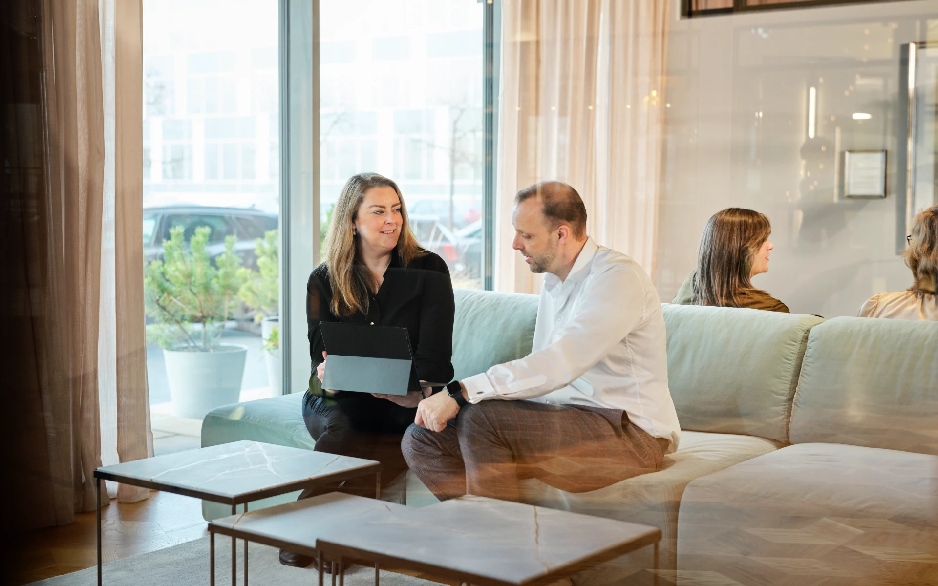 Two colleagues having a conversation in a modern office lounge with a tablet open