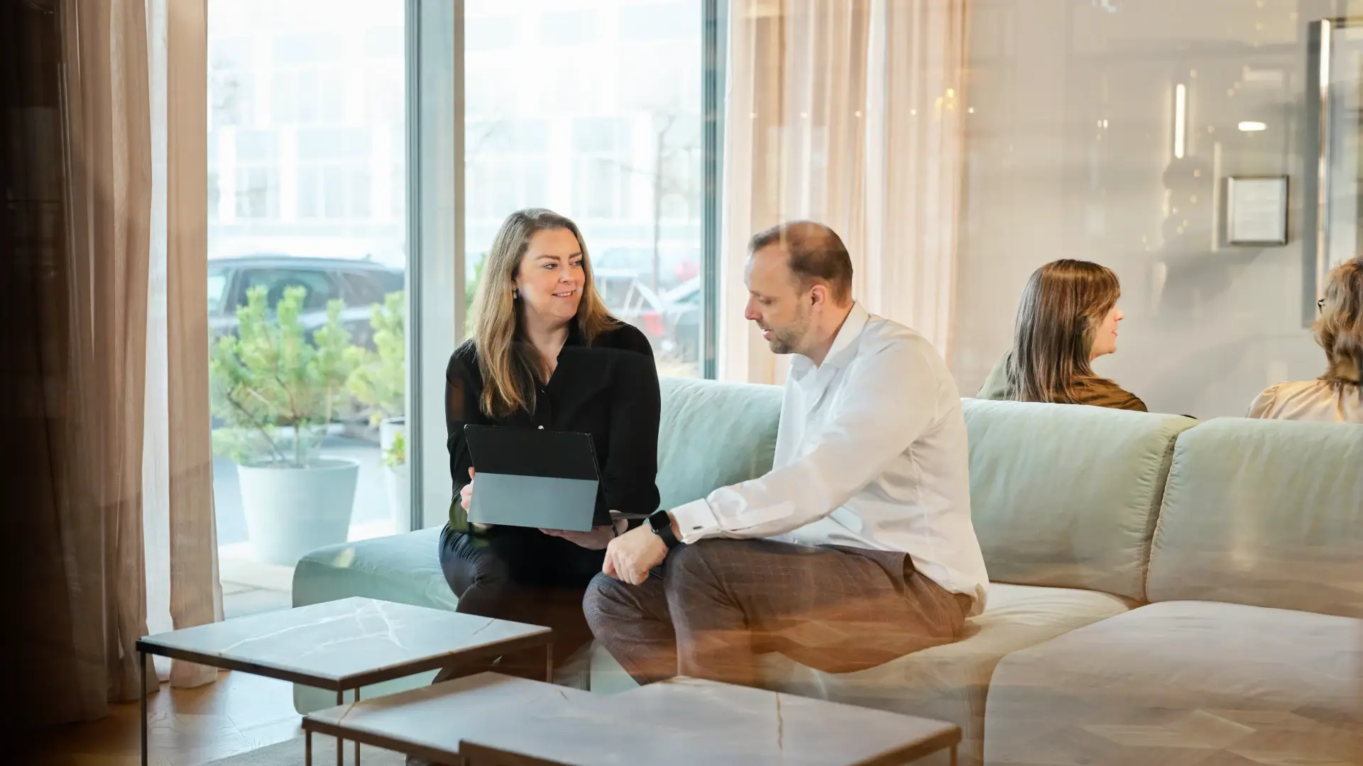 Two colleagues having a conversation in a modern office lounge with a tablet open