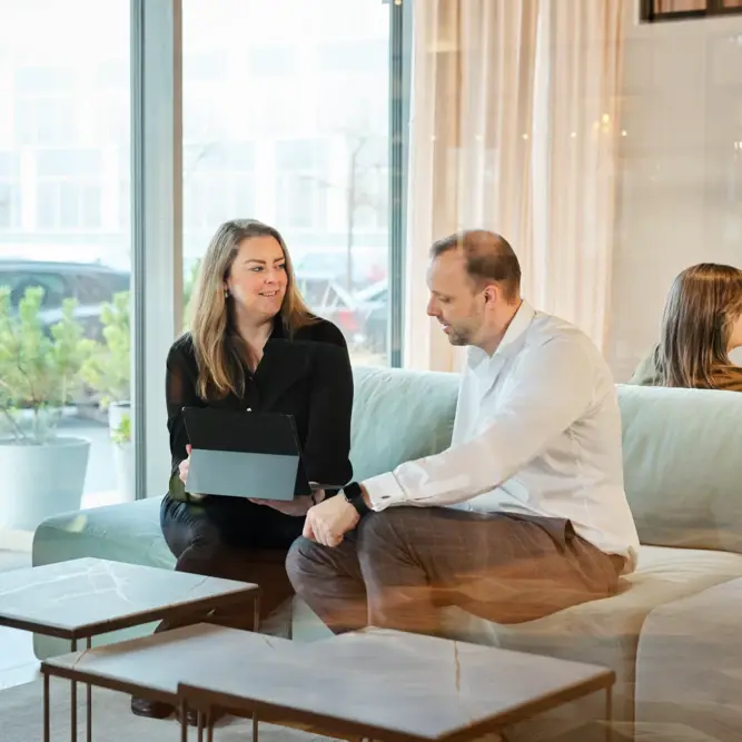 Two colleagues having a conversation in a modern office lounge with a tablet open
