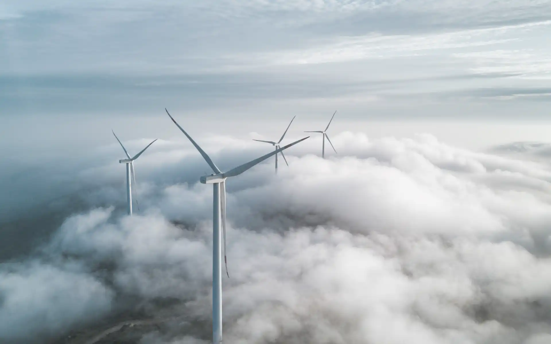 Wind turbines emerging above the clouds in a dramatic, high-altitude setting.