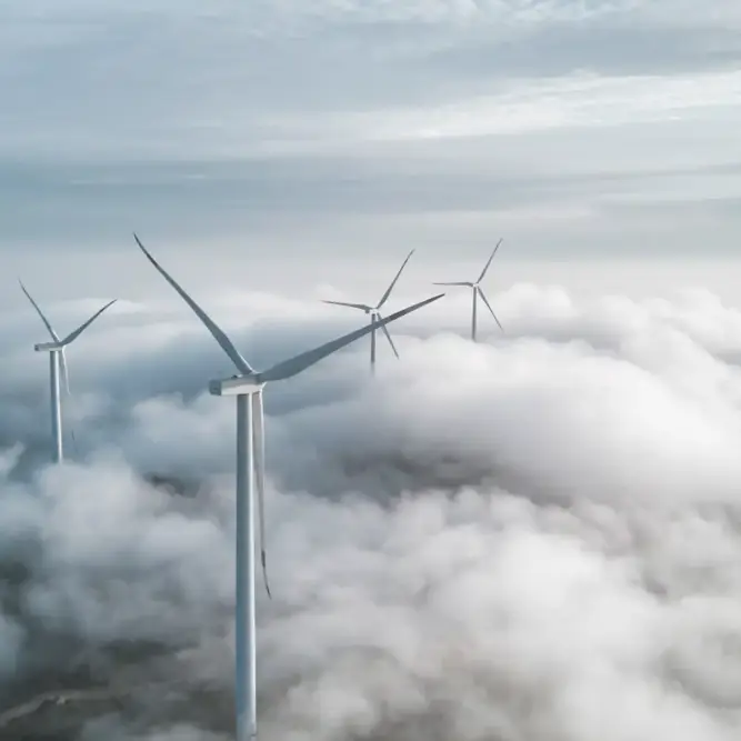 Wind turbines emerging above the clouds in a dramatic, high-altitude setting.