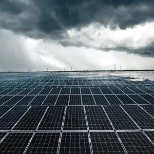 Large solar farm with rows of panels under a dramatic, cloud-filled sky.