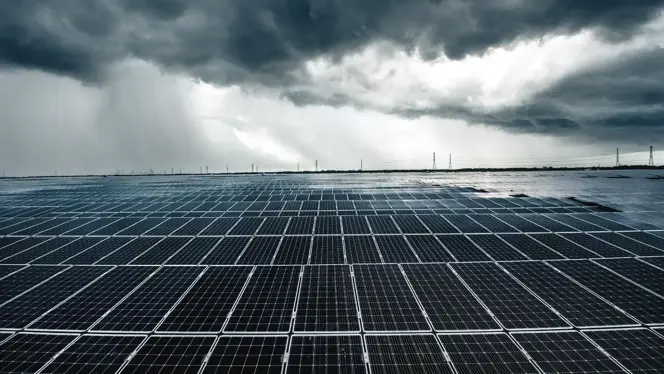 Large solar farm with rows of panels under a dramatic, cloud-filled sky.