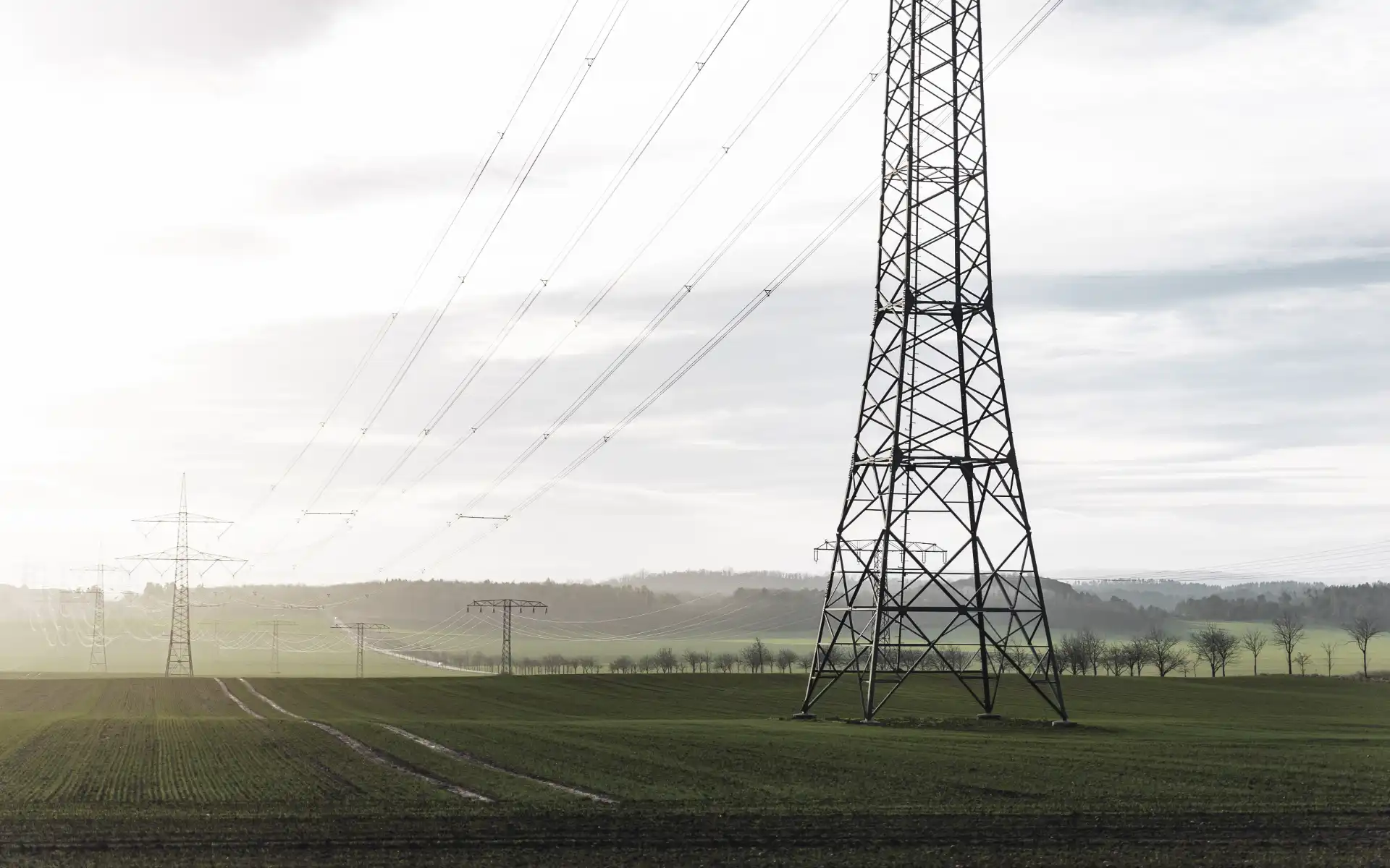 High-voltage transmission towers and power lines stretching across a green rural landscape.