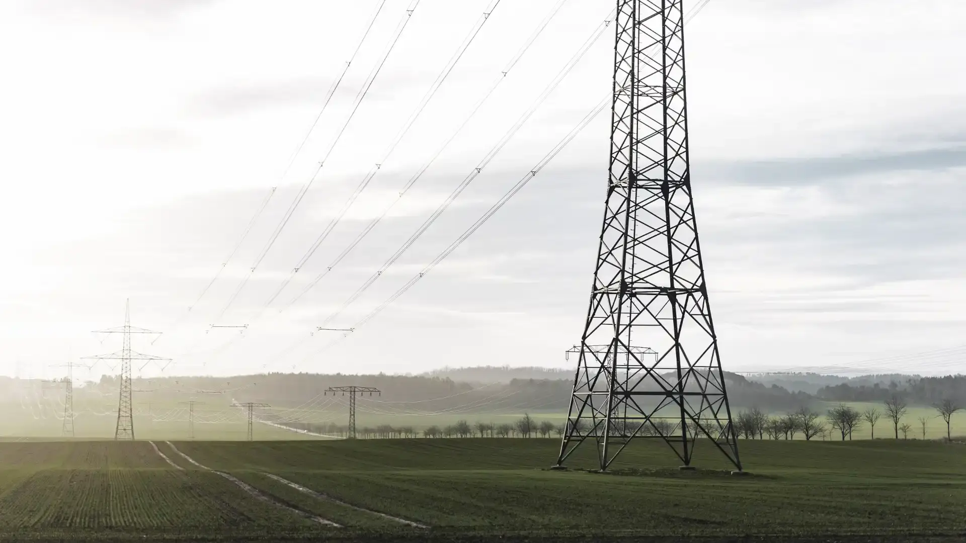 High-voltage transmission towers and power lines stretching across a green rural landscape.