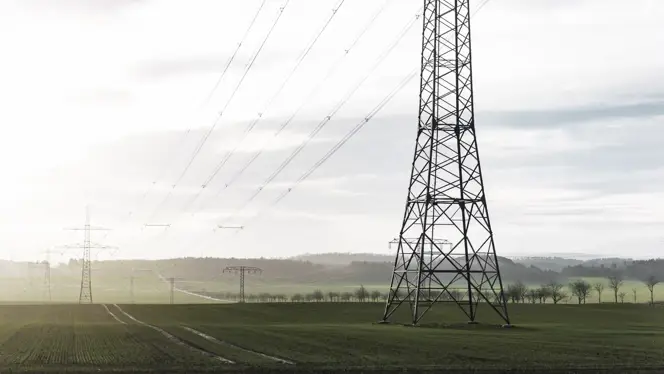 High-voltage transmission towers and power lines stretching across a green rural landscape.