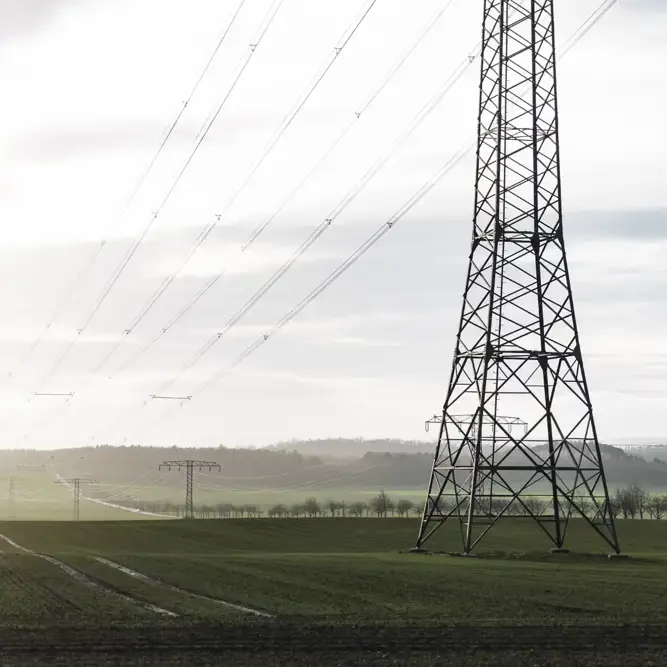 High-voltage transmission towers and power lines stretching across a green rural landscape.