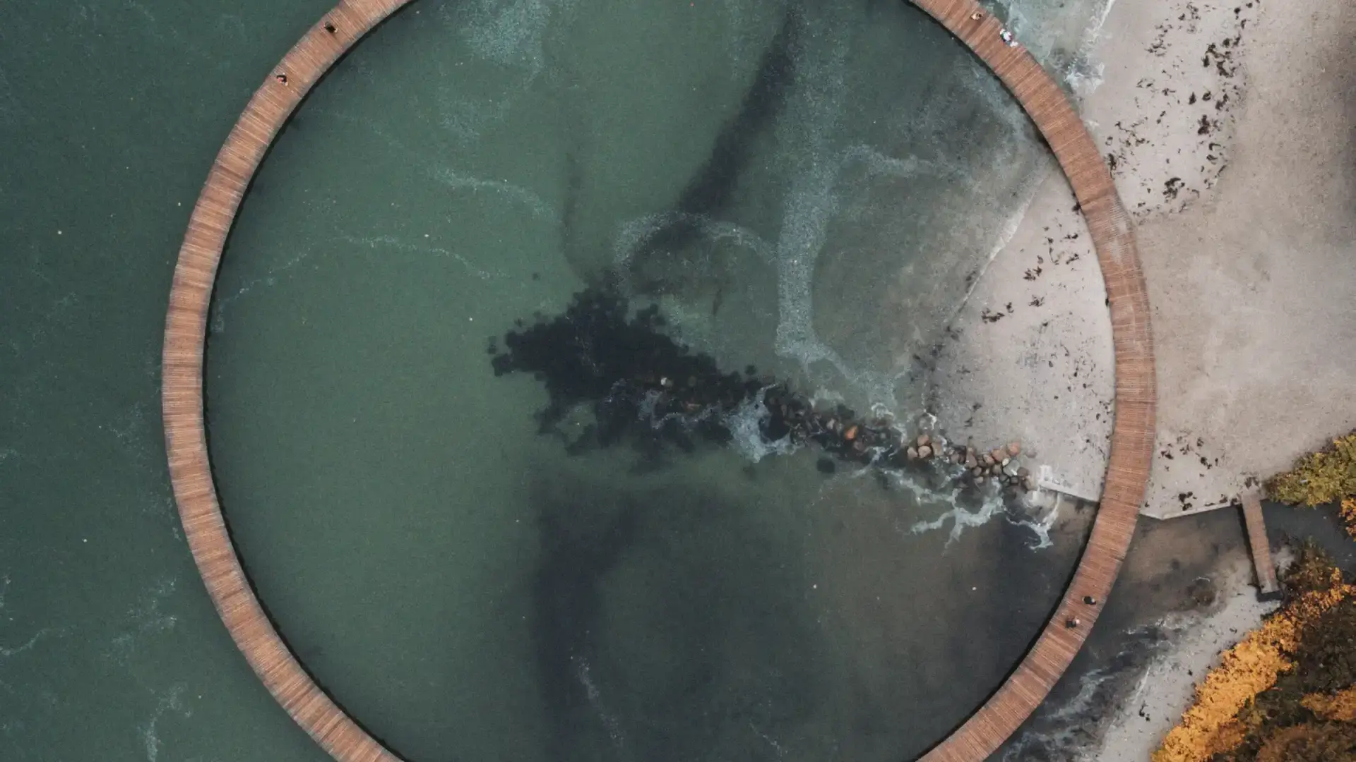 Aerial view of a circular coastal boardwalk over green sea water, symbolizing sustainability, circular economy, and innovative energy pathways.